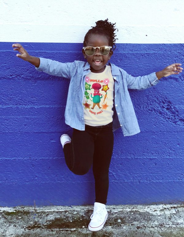 Black girl child, age 5–6, wearing a natural colour T-shirt with Mr Cutesy Myllo design, smiling and playful